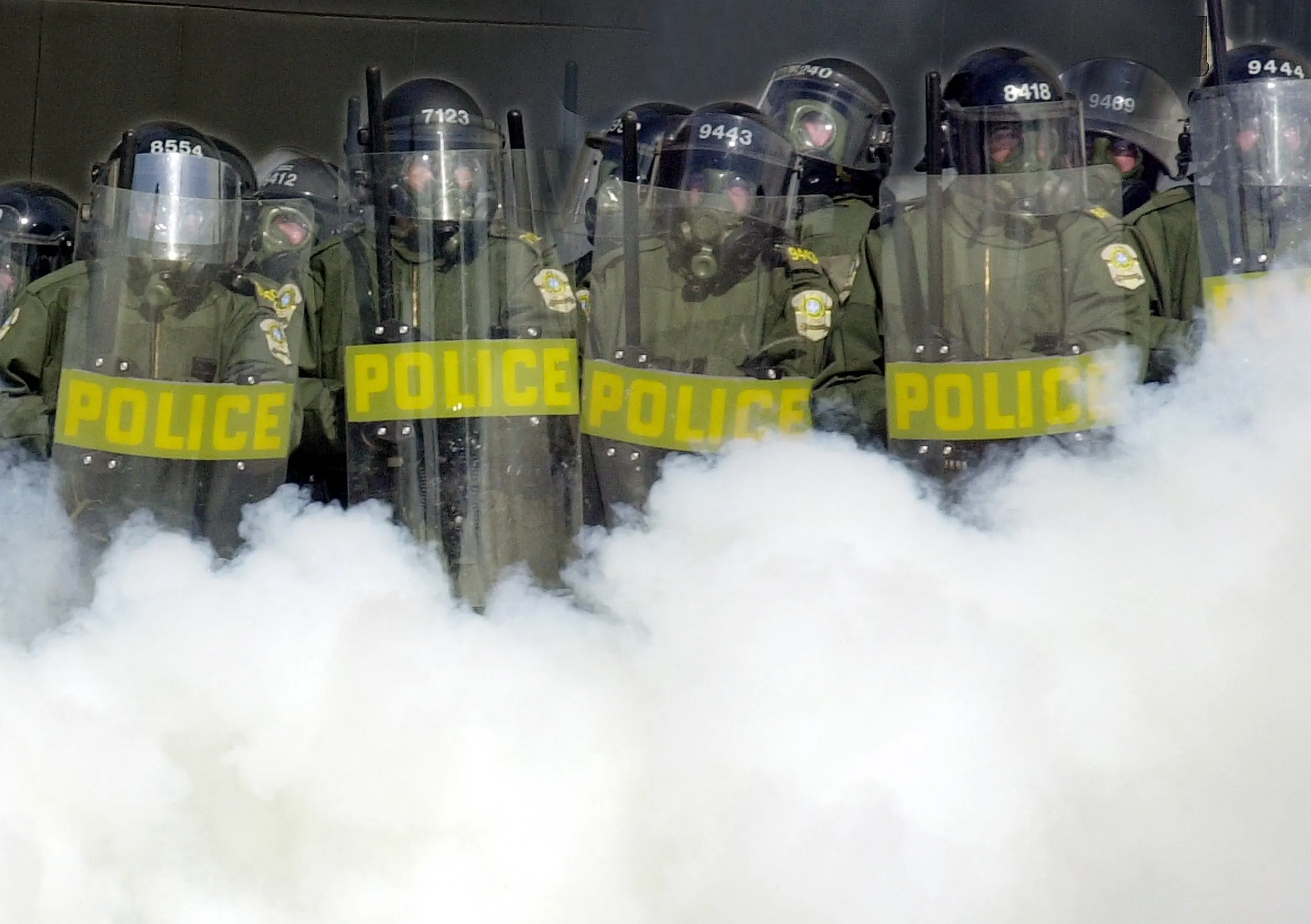 Gaseous Gate — A cloud of tear gas envelops a group of policemen dressed in riot gear as they move in to protect a gate in the security fence surrounding the Summit of the Americas from protesters in Quebec City, Canada, on Saturday afternoon, April 21, 2001. Confrontations between police and protesters continued for a second day while 34 heads of state from the western hemisphere gathered to discuss the possibility of creating the world's largest free trade zone.  (AP Photo/Stephan Savoia)  © The Associated Press