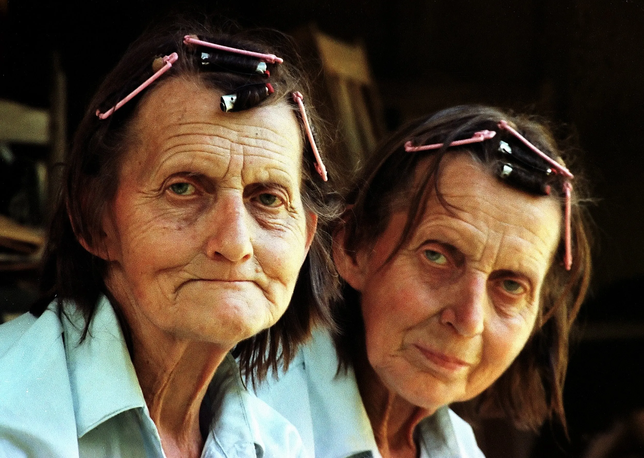 Identiciales — Sixty-seven year old identical twin sisters Dorothy, left, and Doris Barron sit on the porch of their remote ninety-year-old farmhouse where they live with their mother Mary, 91, Dorothy’s daughter Jolene, 37, a 30 year-old cow named “Beggar” and their dog “Spuds.” The women are self-sufficient, drawing water from a nearby stream, growing their own vegetables, raising their own chickens, chopping their own firewood and milking their own goats. The home was built by Dorothy and Doris’ grandfather in 1900 on a hill just north of Pollock, Louisiana in the Kisatchie National Forest.  (Photo by Stephan Savoia)  Published by The Baton Rouge Louisiana State-Times & Morning Advocate on August 6, 1990