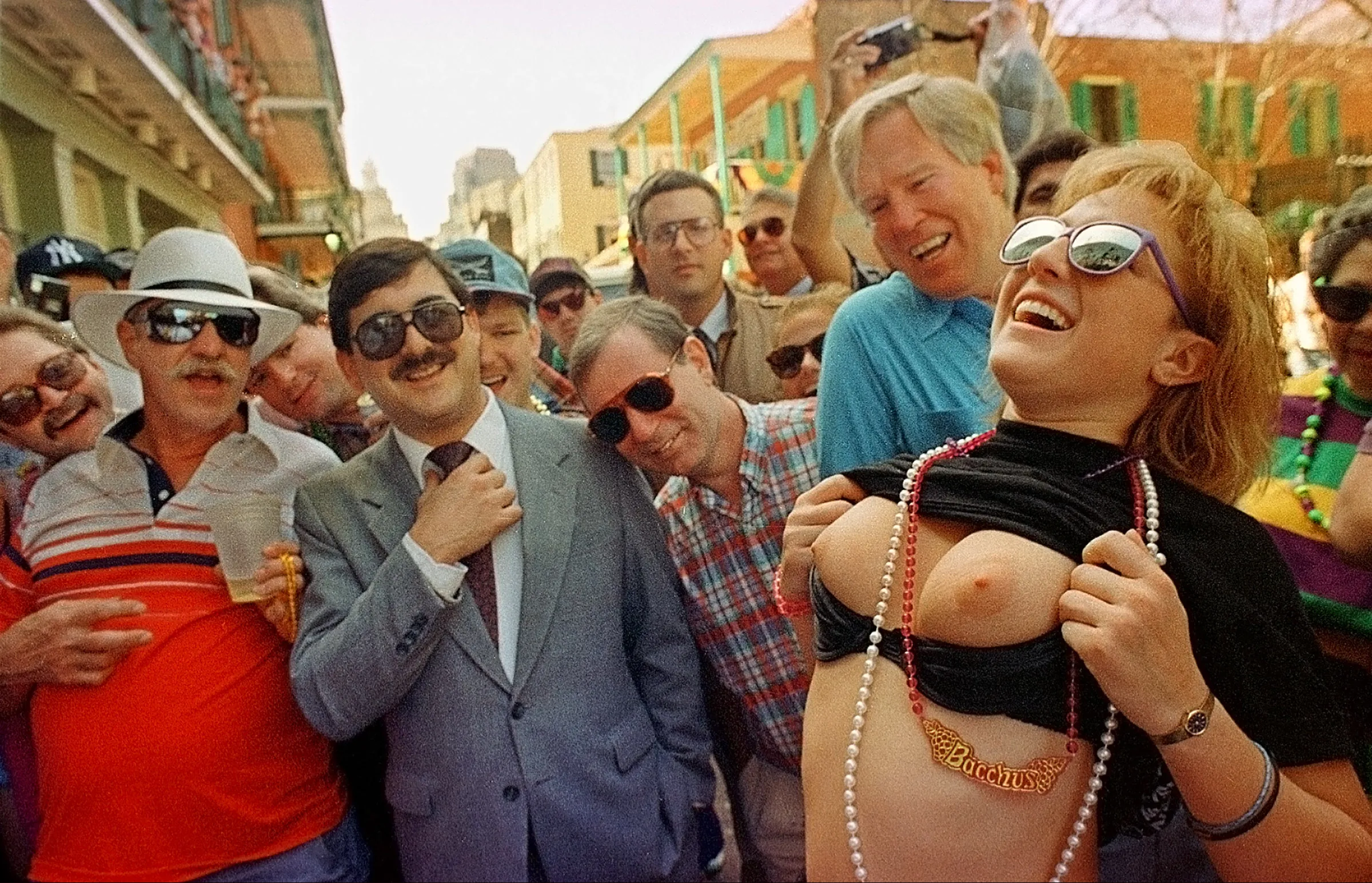 “Laissez Les Bon Temps Rouler!” — A woman reveler passing under a Bourbon Street balcony responds to calls from Mardi Gras celebrants above in exchange for strings of plastic beads during Fat Tuesday celebrations in New Orleans, LA., Tuesday, March 3, 1992. A gaggle of mostly older generational men look on with unobtainable interest.  (AP Photo/Stephan Savoia)  © The Associated Press