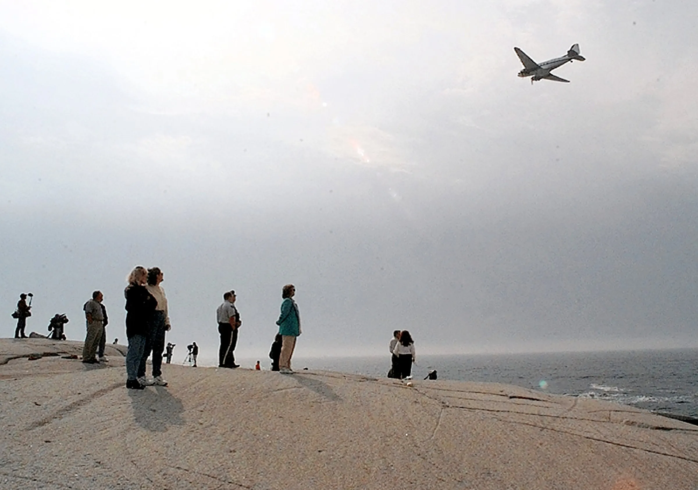 Loss — Loved ones and family members of the casualties in the crash of Swissair Flight 111 look out onto the North Atlantic Ocean crash site from the rocks and boulders of Peggy's Cove, Nova Scotia as a search and recovery aircraft flies overhead Monday, September 8, 1998. The ill-fated Swissair MD-11 jetliner crashed into the Atlantic Ocean some five miles off the coast of Peggy's Cove Wednesday, September 2, 1998 killing all 229 souls aboard.  (AP Photo/Stephan Savoia)  © The Associated Press