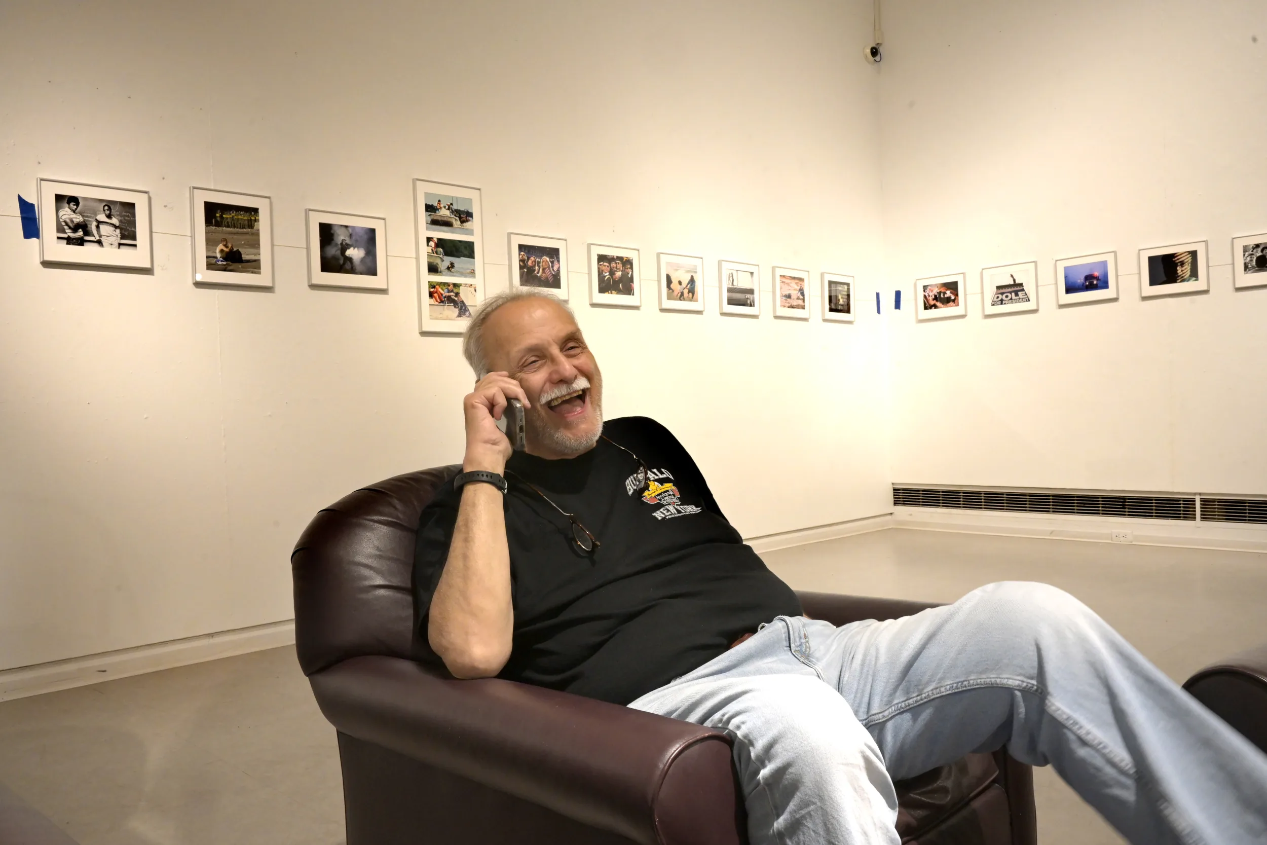 Catching Up — Stephan Savoia laughs as he talks on the phone while reconnecting with an old friend. After many months of work, Stephan can relax a bit as he hangs the inaugural show, “f4 & See It: A Lifetime of Photojournalism,” in the Gibson Gallery at his alma mater, SUNY Potsdam. Thanks to the support of many family and friends. July 6th, 2026  (Photo by Stan Alost)